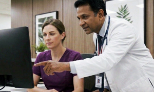 A female nurse and male doctor look over a computer screen reviewing orders for nursing home patients.